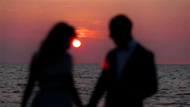 Couple-holding-hands-at-sunset-sea-background-love-silhouetted-close-up.-Unrecognizable-blur-honeymoon-man-and-woman-stand-posing-in-setting-round-sun-pink-sky-ocean-waves-backlit-romantic-surrounding