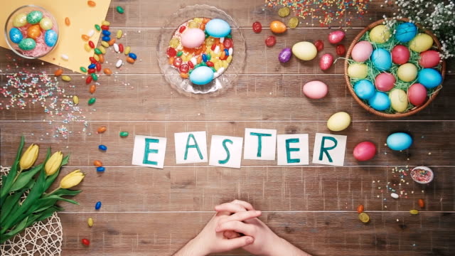 Man-puts-word-Easter-on-table-decorated-with-easter-eggs.-Top-view