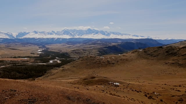 A-flight-over-a-beautiful-valley-with-snowy-mountains-in-the-distance