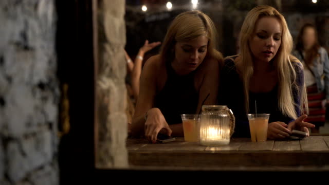 Blonde-girls-drinking-cocktails,-using-smartphones,-obsessed-with-social-media