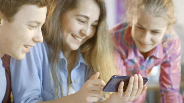 Chico-y-dos-chicas-que-trabajan-en-un-proyecto-de-clase-de-Ciencias-de-las-escuelas-ven-Videos-populares-en-Smartphone.