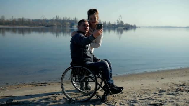 Disabled-man-and-girl-takes-pictures-(selfie),-smiling-man-and-woman-near-river