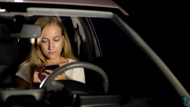 Lächelnde-Frau-mit-Smartphone-im-Auto-in-der-Nacht