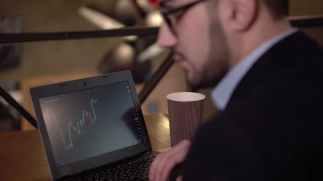 Young-man-trader-with-a-beard-stops-to-study-cryptocurrency-market-and-removes-glasses-after-tired-and-hard-work