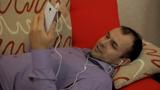 Junger-Mann-mit-video-Chat-mit-Smartphone-Webcam-Chat-Freundin-liegen-auf-dem-Sofa-zu-Hause-entspannen.