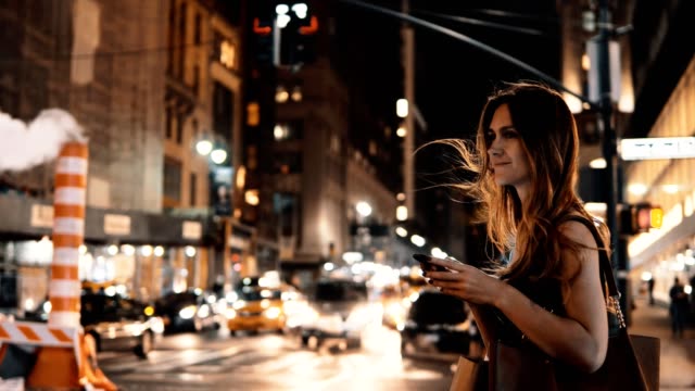 Mujer-hermosa-joven-en-la-noche-en-el-centro-de-tráfico-y-con-el-smartphone-en-Nueva-York,-América