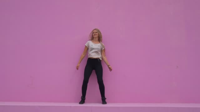 Casual-girl-with-braided-hair-having-fun-and-silly-dancing-over-pink-background