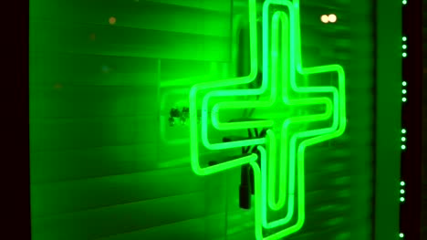 panning-of-marijuana-dispensary-neon-green-weed-cross-on-city-store-front-window