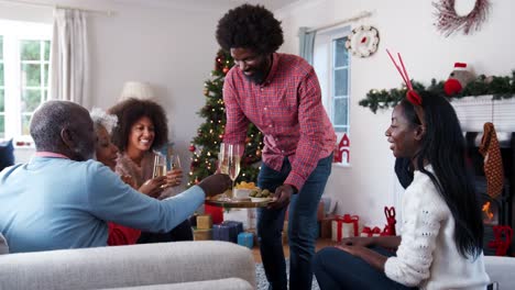 Mann-mit-Champagner-und-Snacks-wie-Erwachsene-Mitglieder-der-Familie-Weihnachten-zu-Hause-feiern