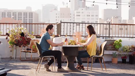 Paar,-trinken-Wein-und-Toast-auf-Dachterrasse-mit-Skyline-der-Stadt-im-Hintergrund