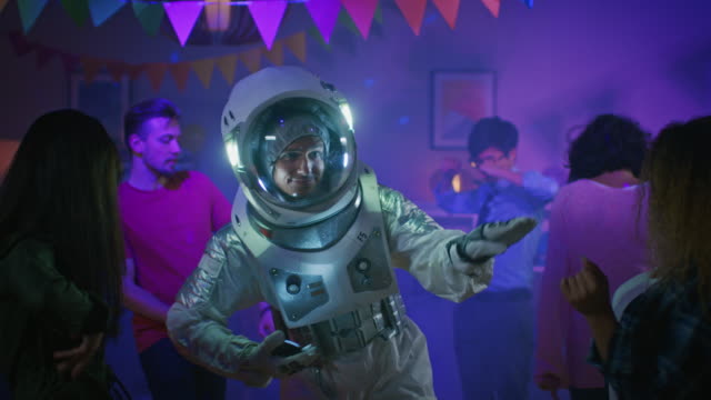 At-the-College-House-Costume-Party:-Fun-Guy-Wearing-Space-Suit-Dances-Off,-Doing-Groovy-Funky-Robot-Dance-Modern-Moves.-With-Him-Beautiful-Girls-and-Boys-Dancing-in-Neon-Lights.-In-Slow-Motion.