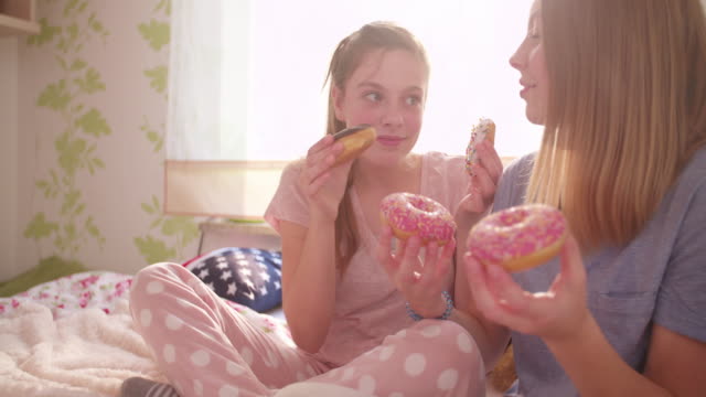 Riendo-teen-girls-compartir-rosquillas-en-un-amplio-dormitorio