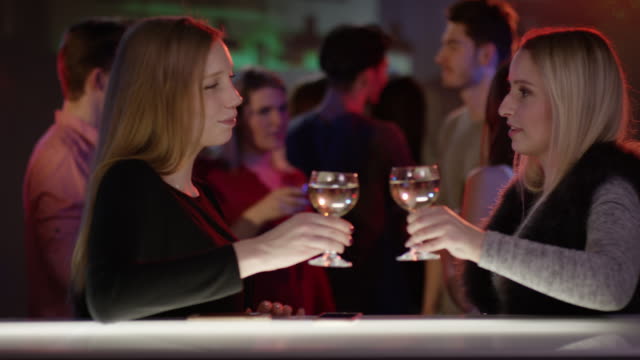 two-attractive-girls-at-bar-in-club-talking-and-raising-their-glasses