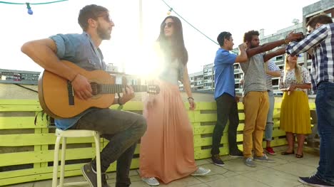 Musician-playing-guitar,-group-of-people-taking-photos-at-rooftop-party