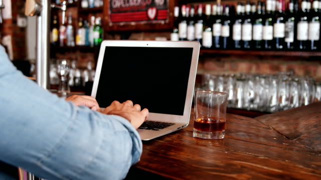Man-using-laptop-while-having-whisky-at-counter