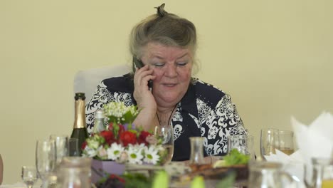 Ältere-Frau-am-festlich-gedeckten-Tisch-am-Telefon-sprechen