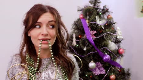 Girl-tired-to-decorate-Christmas-tree,-garland-in-the-mouth