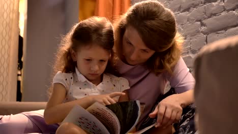 Mutter-süßen-Töchterchen-Buch-zu-lesen-und-sitzen-zusammen-im-modernen-Wohnzimmer,-Familienkonzept,-drinnen