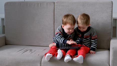 Two-twin-brothers-take-away-each-other's-tablet-sitting-on-the-sofa.-Kids-play-games-on-the-tablet.
