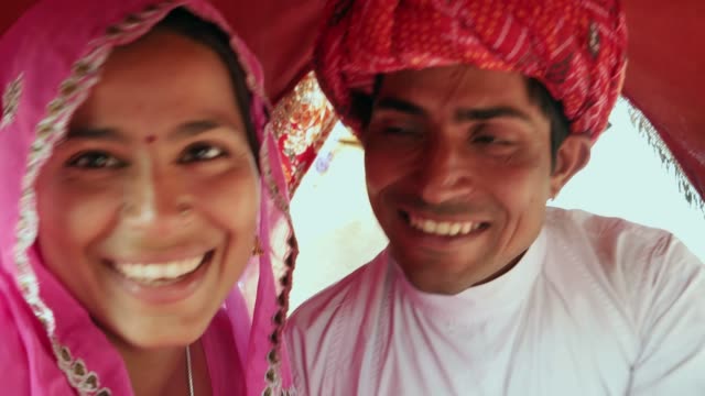 Rajasthani-Paar-in-ethnischen-Kleid-genießen-ein-Kamel-reiten-in-einem-Wohnwagen-auf-Messe-Pushkar,-Rajasthan,-Indien