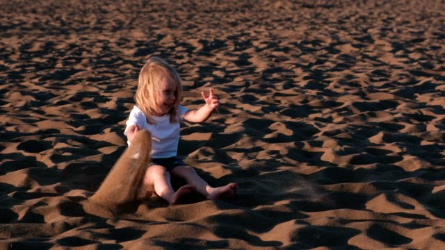 Beautiful-happy-little-girl-blonde-playing-and-throwing-sand-on-the-beach.