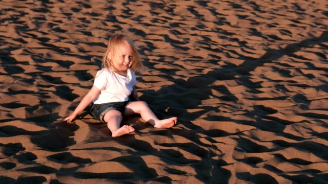 Girl-playing-in-the-sand-sitting-on-the-beach.