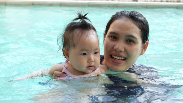 Asiatische-junge-Mutter-und-liebenswert-lockiges-kleines-Mädchen-Spaß-in-einem-Schwimmbad.