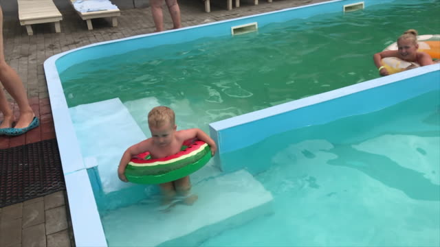 Ein-kleiner-Junge-und-ein-junges-Mädchen-im-Pool-toben-auf-aufblasbaren-Kreisen.