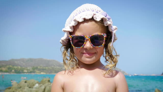 Portrait-of-beautiful-little-girl-having-fun-on-the-sea,-cute-smiling-in-panama,-sun-protection-cream,-background-of-sea-blue-water-and-rocks.