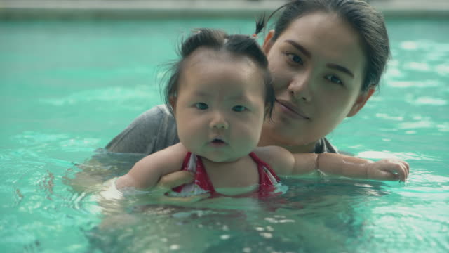 Asiatische-junge-Mutter-und-liebenswert-lockiges-kleines-Mädchen-Spaß-in-einem-Schwimmbad.