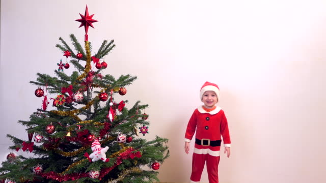Glückliches-Kind-gekleidet-an-den-Weihnachtsmann-springen-in-der-Nähe-von-Weihnachtsbaum,-Geschenke-warten