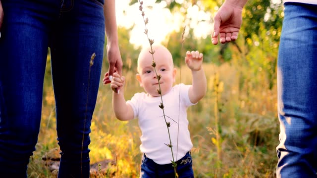Close-up-portrait-of-the-baby.-Kid-is-walking-on-the-grass-in-the-forest,-parents-are-holding-his-hands