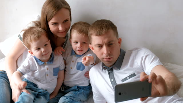 Dad-makes-family-selfie-on-mobile-phone.-Mom,-dad-and-two-brother-twins-toddlers.