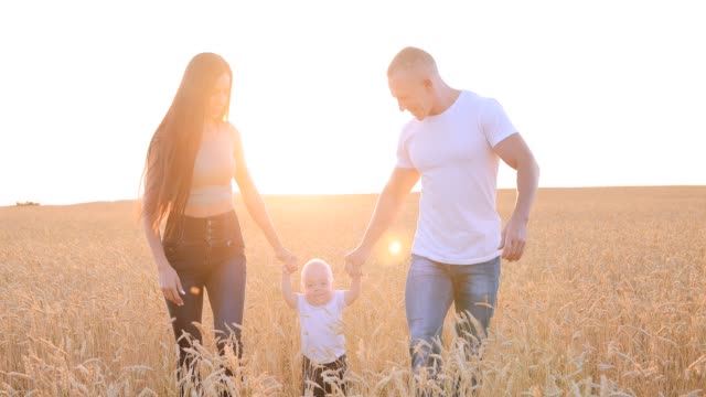 Happy-parents-hold-the-little-son-by-the-hand-and-raise-her-high,-playing-with-him.-Happy-family-in-a-wheat-field