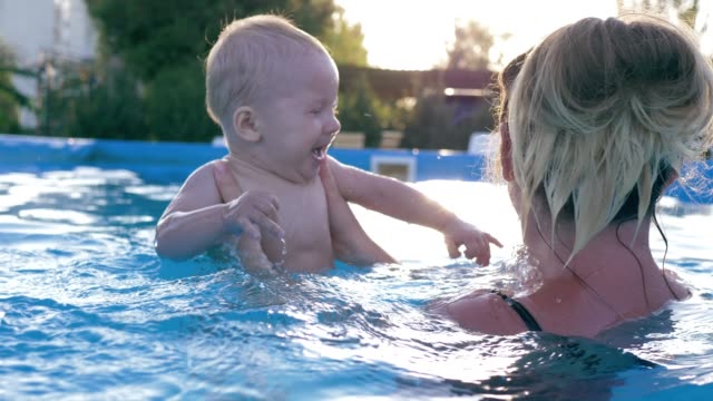 happy-infant-doing-splashes-in-swimming-pool,-small-boy-with-mother-have-fun-at-summer-hot-day