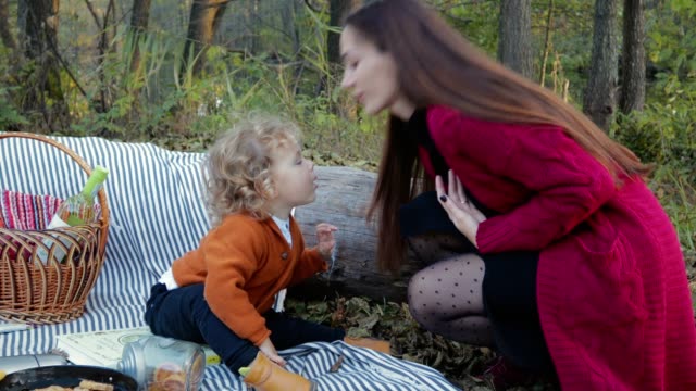 Glückliche-Mutter-ihr-Kind-auf-ein-Picknick-im-Wald-küssen-und-gibt-ihm-das-Telefon