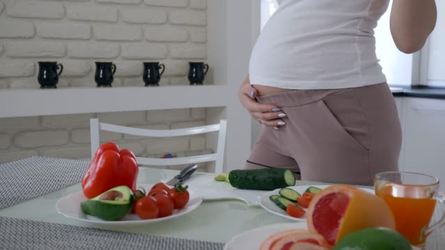 Schwangerschaft-Frau-mit-großen-Bauch-ist-nützlichen-leckeren-Salat-aus-frischem-Gemüse-für-gesundes-Essen-in-der-Küche-kochen