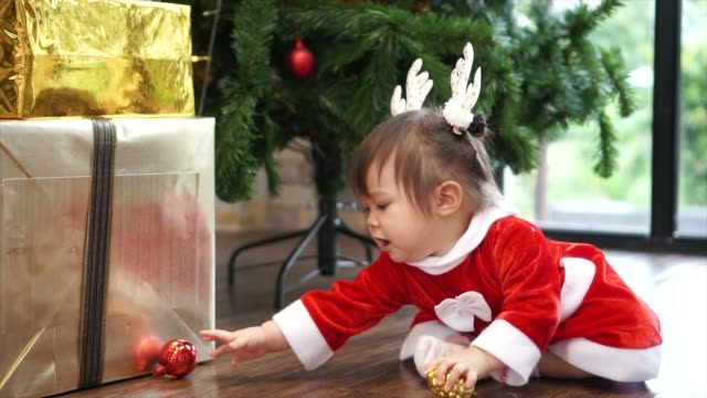 Cute-1-year-old-baby-girl-wearing-reindeer-headband-playing-with-Christmas-ornament-with-christmas-tree-in-background.-Merry-Christmas-and-Happy-Holidays!