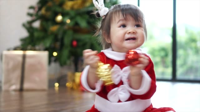Niedliche-1-Jahr-alt-Baby-Mädchen-tragen-Rentier-Haarreif-mit-Christbaumkugel-mit-Weihnachtsbaum-im-Hintergrund-zu-spielen.-Frohe-Weihnachten-und-schöne-Feiertage!