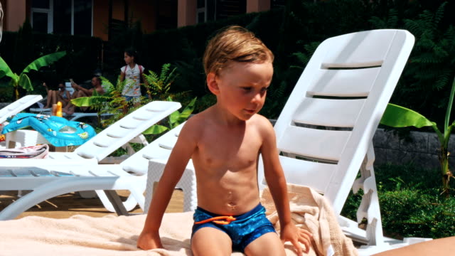 Happy-little-boy-sitting-near-the-pool