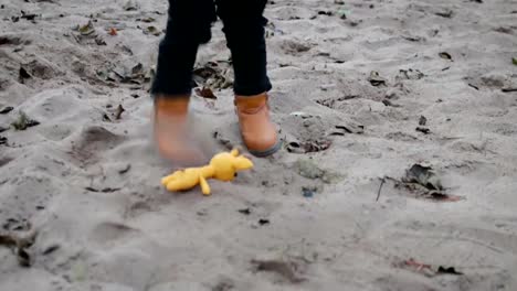Eine-kleine,-lockige-junge-läuft-über-den-Sand-auf-dem-Spielzeug