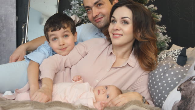Junge-Familie-mit-Sohn-und-Neugeborenen-liegen-auf-einem-Bett-in-Weihnachten