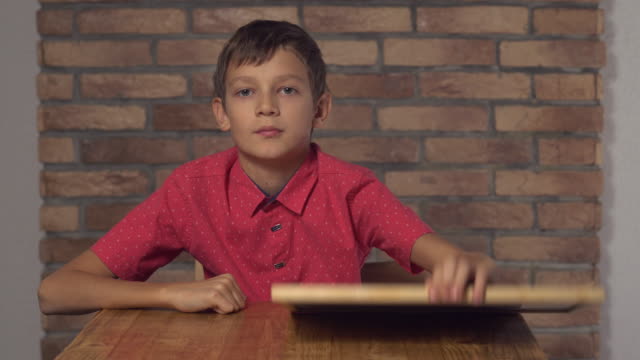 niño-sentado-en-el-escritorio-sosteniendo-el-rotafolio-con-letras-como-en-el-fondo-de-pared-de-ladrillo-rojo