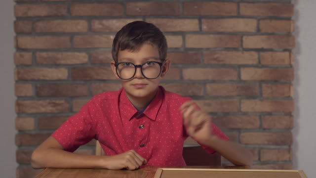 Kind-sitzt-am-Schreibtisch-mit-Flipchart-mit-Schriftzug-auf-dem-Hintergrund-rote-Backsteinwand