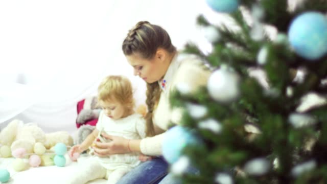 Happy-young-mother-playing-with-her-sweet-baby-in-a-decorated-room-near-the-christmas-tree