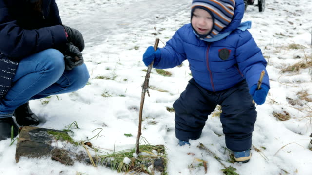 Attractive-baby-playing-with-mother-in-winter-on-the-street.-The-boy-in-the-hands-of-the-branches-of-trees