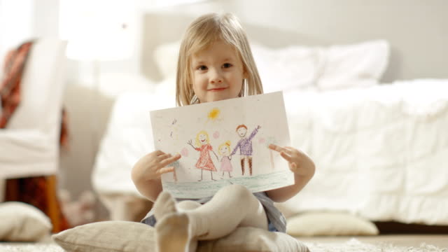 Süße-junge-Mädchen-auf-Kissen-sitzend-zeigt-Zeichnung-von-ihrer-Familie.