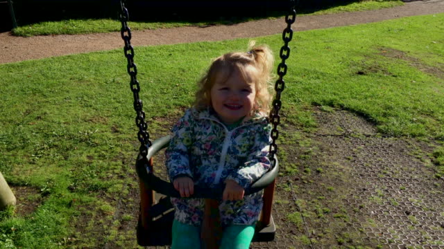 Young-toddler-girl-having-fun-in-the-British-summertime-at-the-park-on-the-swing