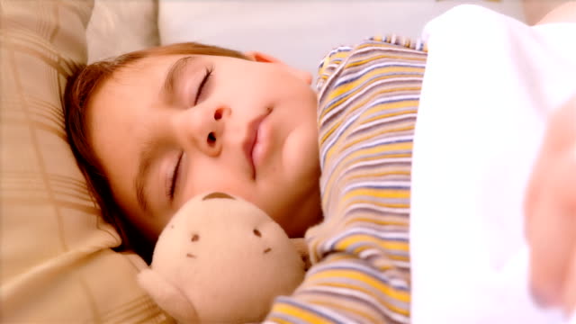 Portrait-of-3-years-old-boy-sleeping-with-teddy-bear.-His-mother-hand-covering-him-with-blanket.