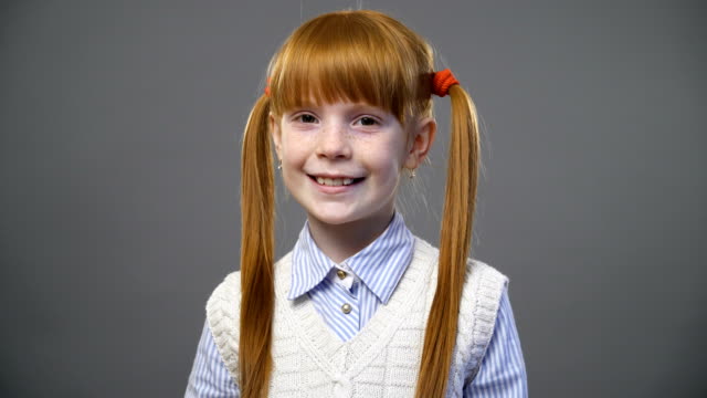 Beautiful-redhead-girl-with-two-pigtails-looking-onto-the-camera-and-smiling-against-gray-background